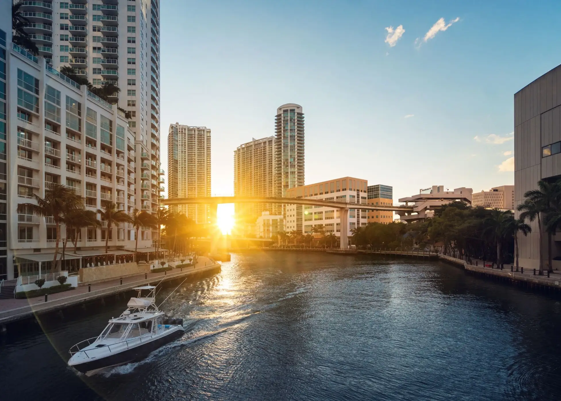 View of the Miami River at sunset with modern buildings and a boat passing by, highlighting urban luxury and lifestyle.